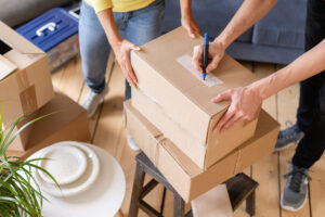 two people packing boxes and using a pen to write what is inside of each box.
